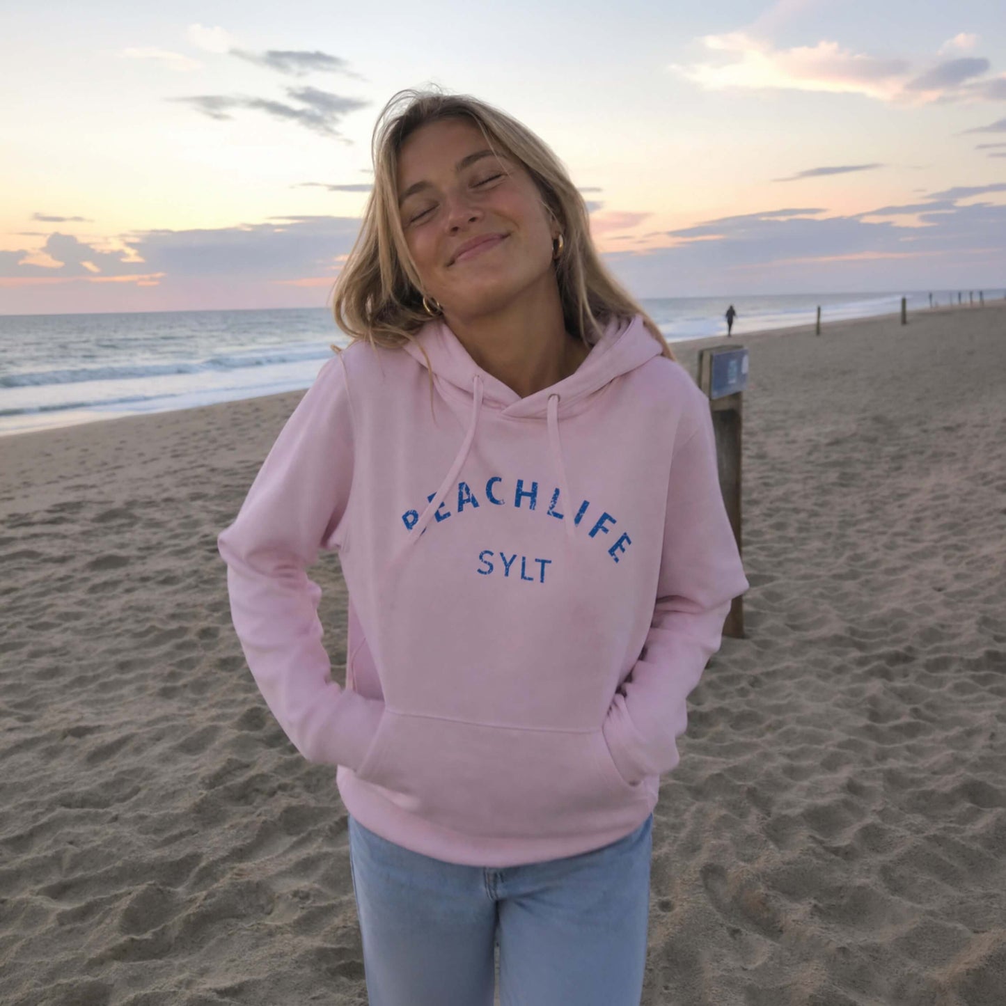 Ein Modell steht am Strand auf Sylt auf Sylt mit einem pinken Sylt Hoodie